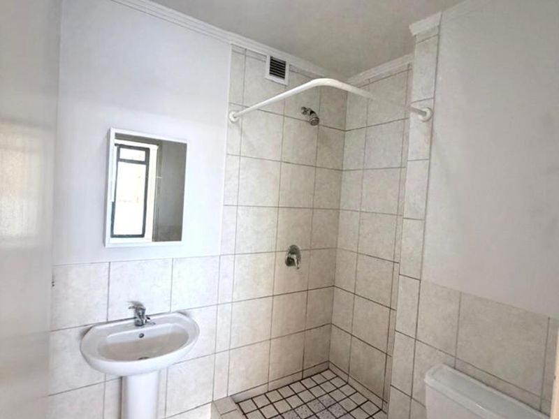 A functional bathroom featuring a pedestal basin, toilet, and a tiled shower cubicle with a raised base.