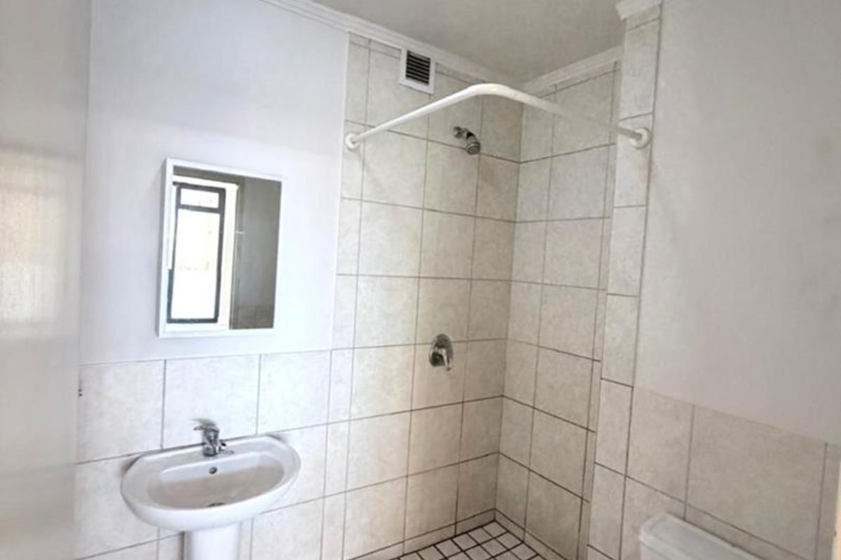 A functional bathroom featuring a pedestal basin, toilet, and a tiled shower cubicle with a raised base.