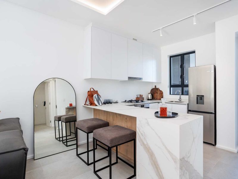 Modern open-plan kitchen featuring a marble-look stone breakfast bar, sleek white cabinetry, integrated appliances, and contemporary track lighting.