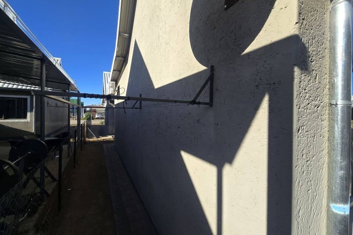 Side exterior walkway of the townhouse featuring a wall-mounted clothesline, paved path, and metal downpipe.