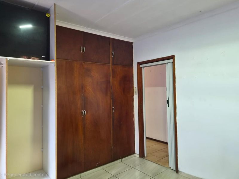 A bedroom featuring built-in wooden cupboards and tiled flooring, offering a blank canvas for potential renovation or restyling.