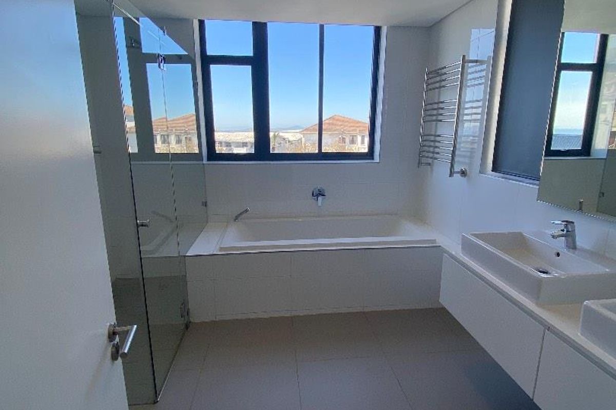 Modern bathroom featuring a built-in bathtub, glass shower enclosure, double vanity, and heated towel rail with large windows offering natural light.
