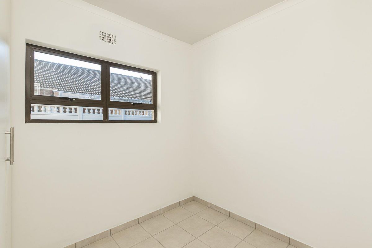A clean, empty bedroom featuring neutral tiled flooring, white walls, and an aluminium-framed window providing natural light.