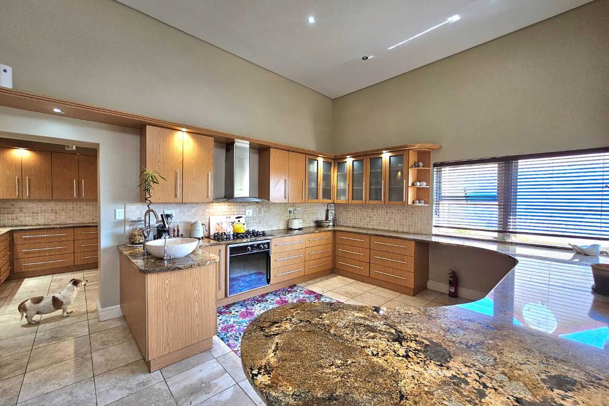 Spacious kitchen featuring light wood cabinetry, granite countertops, a built-in oven, stainless steel extractor fan, and tiled flooring with an adjoining scullery area.