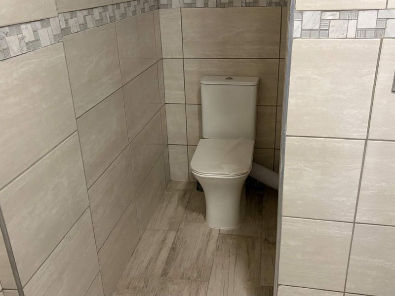 A compact bathroom featuring neutral ceramic wall and floor tiles with a decorative border and a standard white toilet.