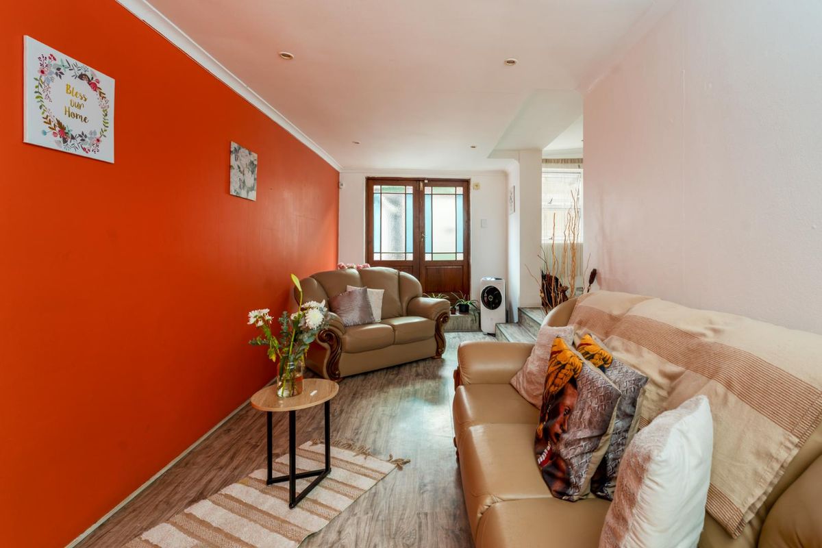 A living room featuring wood-look laminate flooring, recessed ceiling lighting, and a distinctive orange accent wall leading toward a glass-paneled exterior door.