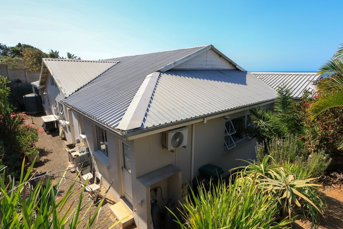 An elevated view of the rear exterior of the farm property, featuring a corrugated metal roof, paved pathways, and established garden surroundings.