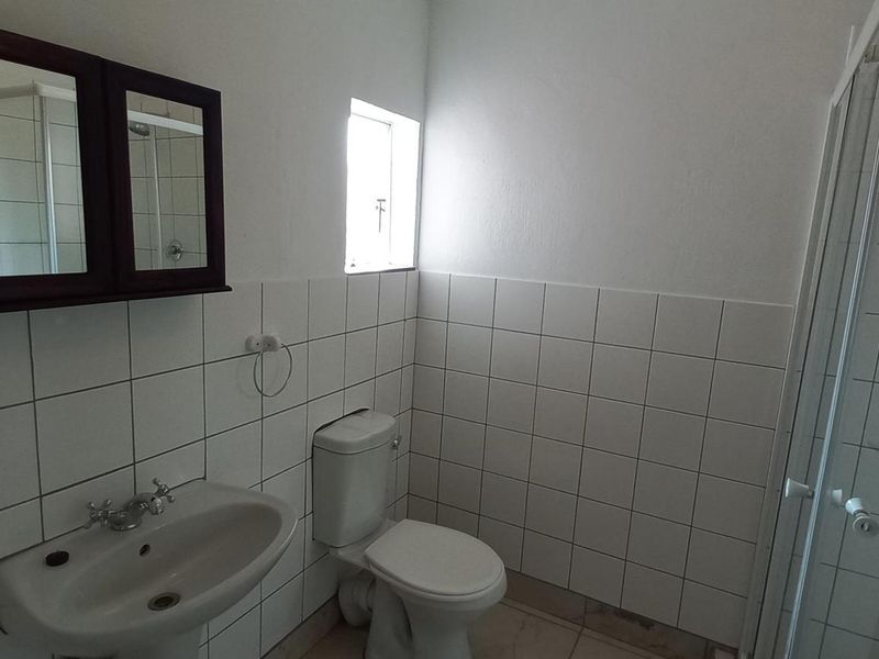A functional bathroom featuring a pedestal basin, toilet, and a glass-enclosed shower with white wall tiling.