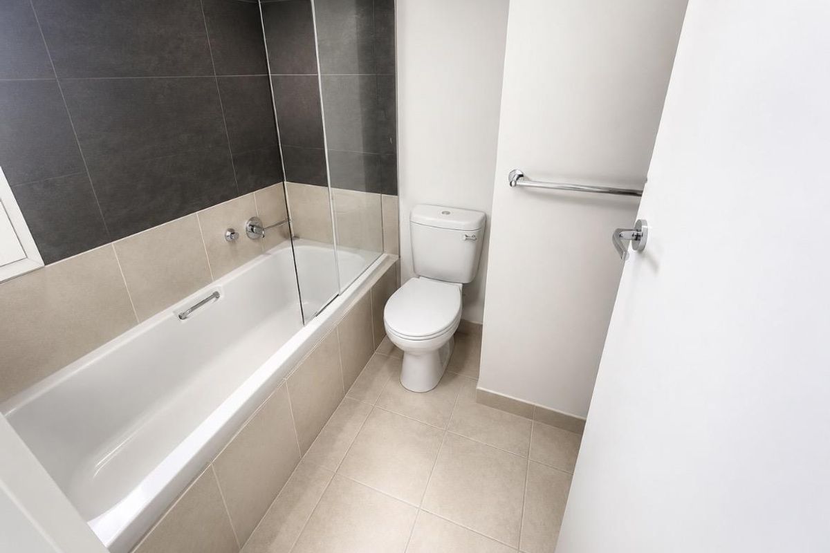A clean, modern bathroom featuring a bathtub with a glass screen, a toilet, and neutral-toned wall and floor tiling.