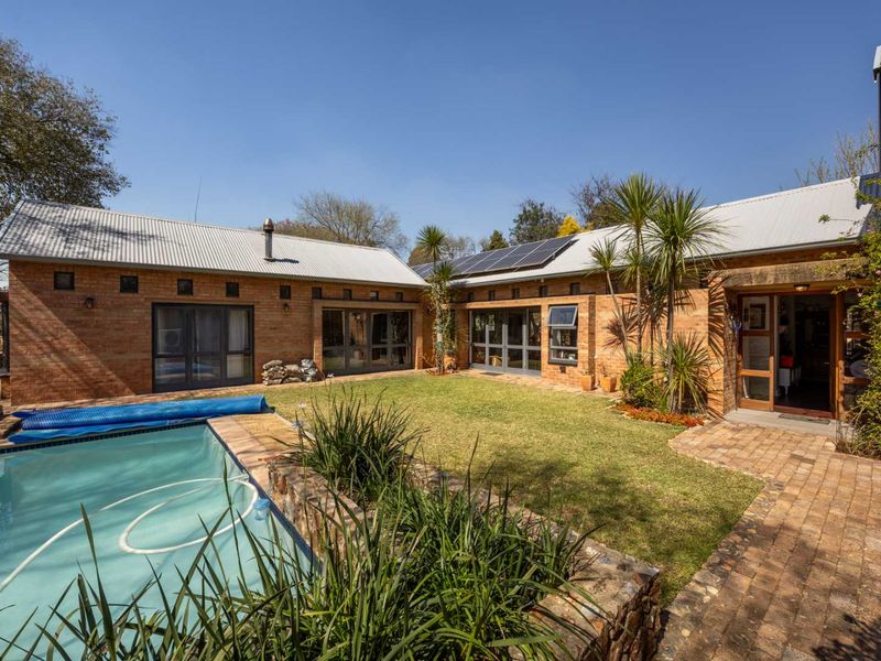Rear view of a brick house featuring a swimming pool, well-maintained lawn, solar panels, and multiple access points through glass doors.