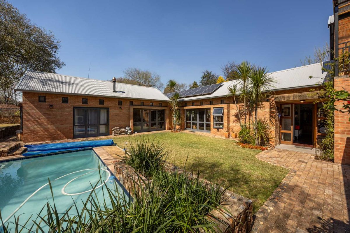 Rear view of a brick house featuring a swimming pool, well-maintained lawn, solar panels, and multiple access points through glass doors.