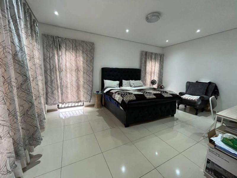 Spacious bedroom featuring neutral tiled flooring, recessed downlighting, and large windows with curtain tracks, offering a clean and functional living space.