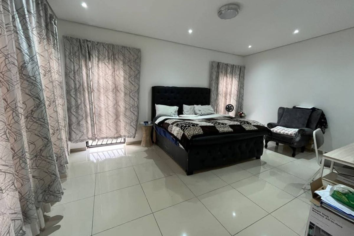 Spacious bedroom featuring neutral tiled flooring, recessed downlighting, and large windows with curtain tracks, offering a clean and functional living space.