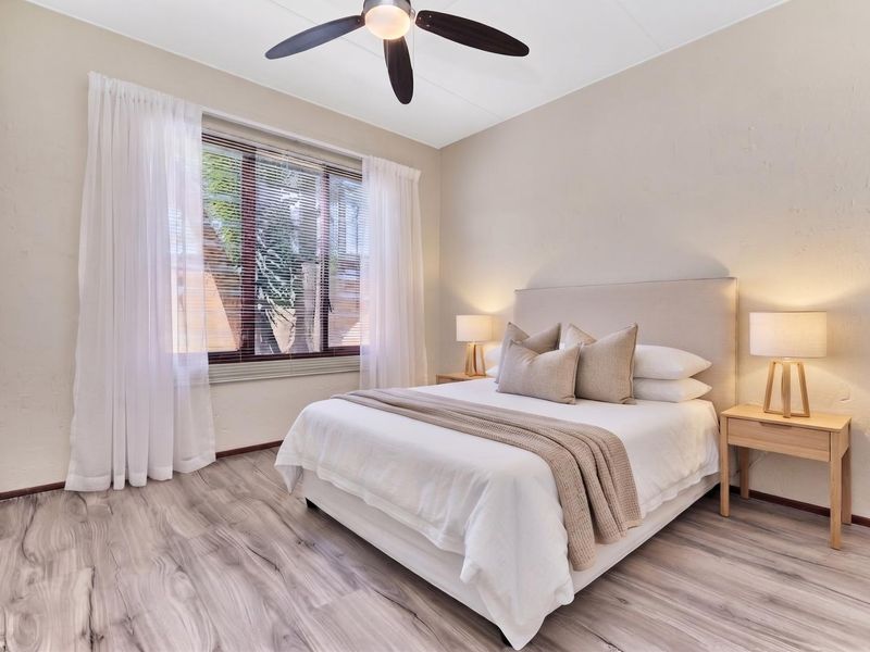 A well-maintained bedroom featuring modern laminate flooring, a ceiling fan, and a built-in cupboard, offering a clean and comfortable living space.
