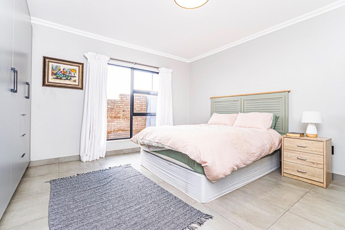 A bright and well-maintained bedroom featuring neutral tiled flooring, a built-in wardrobe, and large windows allowing for natural light.