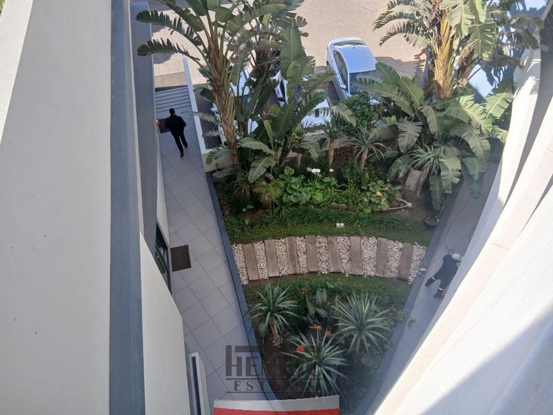 An elevated aerial view of a well-maintained landscaped garden area with a paved walkway and lush greenery within the apartment complex.