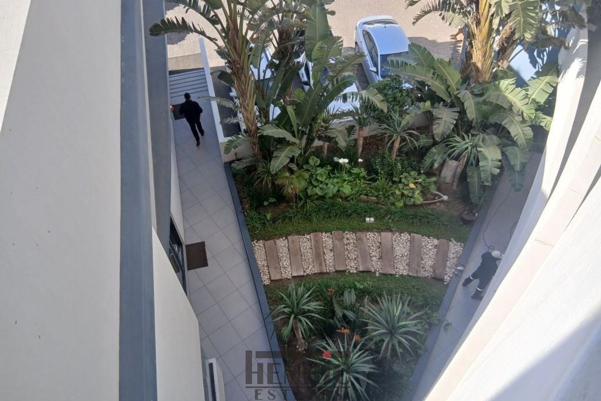An elevated aerial view of a well-maintained landscaped garden area with a paved walkway and lush greenery within the apartment complex.