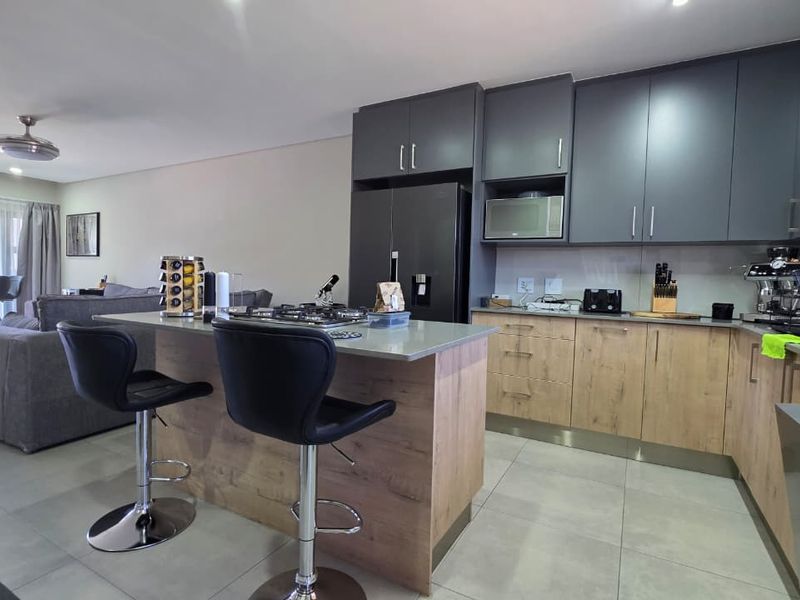 Modern open-plan kitchen featuring two-tone cabinetry, stone countertops, a central island with a gas hob, and integrated appliances, flowing into the living area.