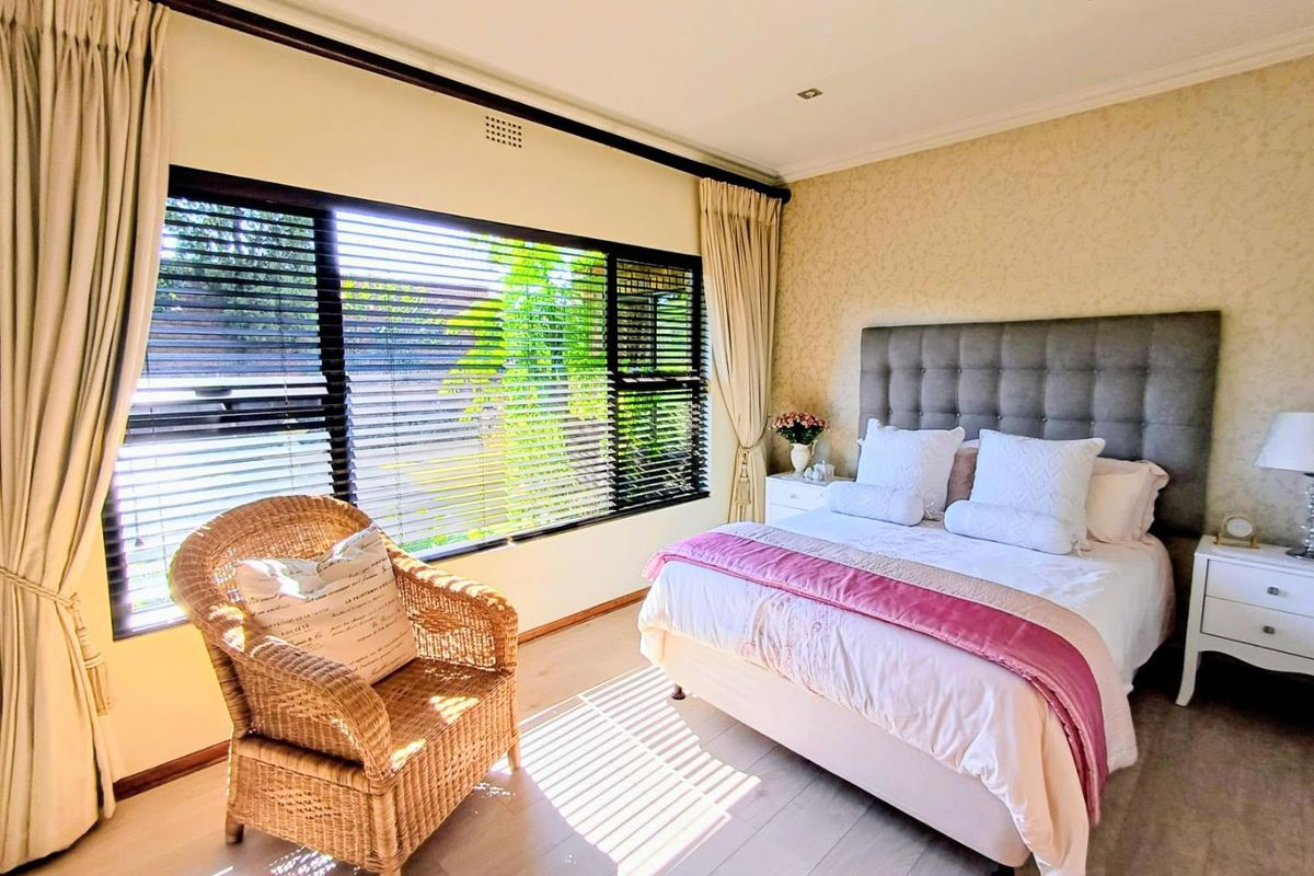 A well-maintained bedroom featuring laminate flooring, recessed downlighting, and large windows fitted with venetian blinds and curtains.