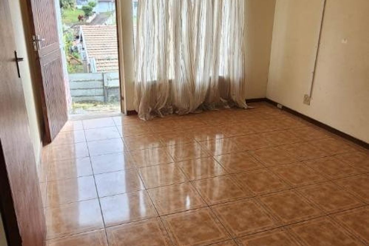 An empty living room featuring ceramic tiled flooring, a ceiling fan, and direct access to the exterior through a wooden door.