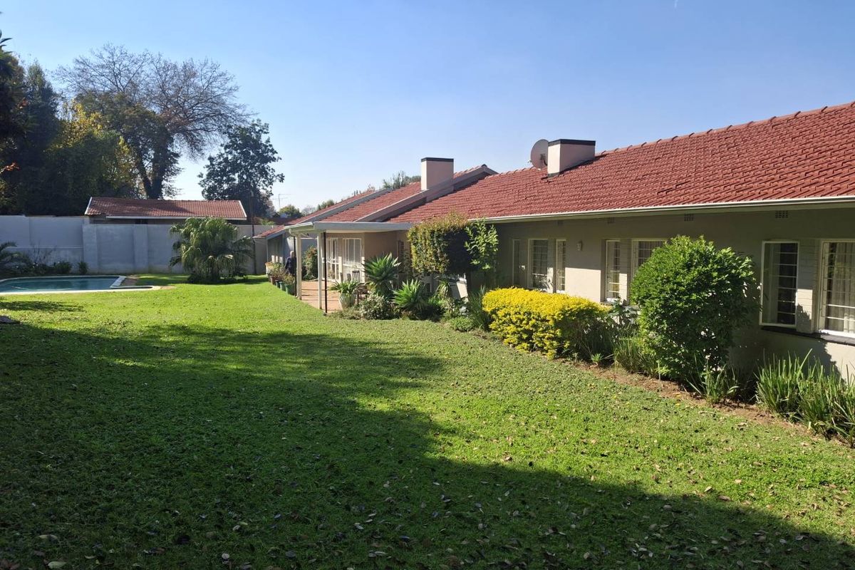 Spacious rear garden featuring a swimming pool, a covered patio area, and a well-maintained lawn alongside the main house structure.