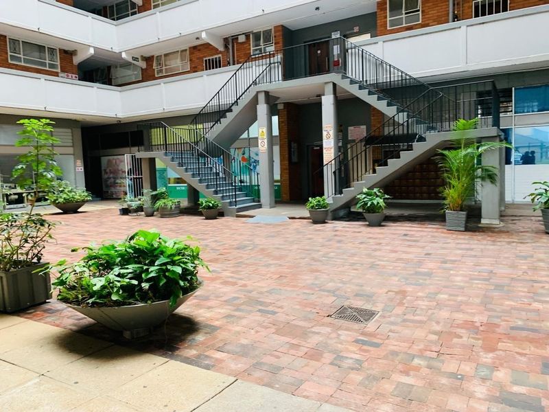 A communal courtyard area featuring brick paving, a central staircase with metal railings, and access to apartment building entrances.