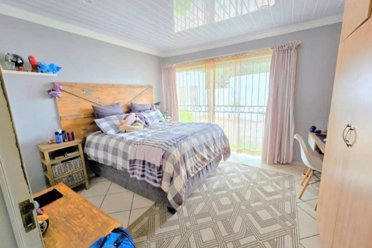 A well-lit bedroom featuring tiled flooring, a built-in wardrobe, and a sliding glass door with security gate providing access to the exterior.