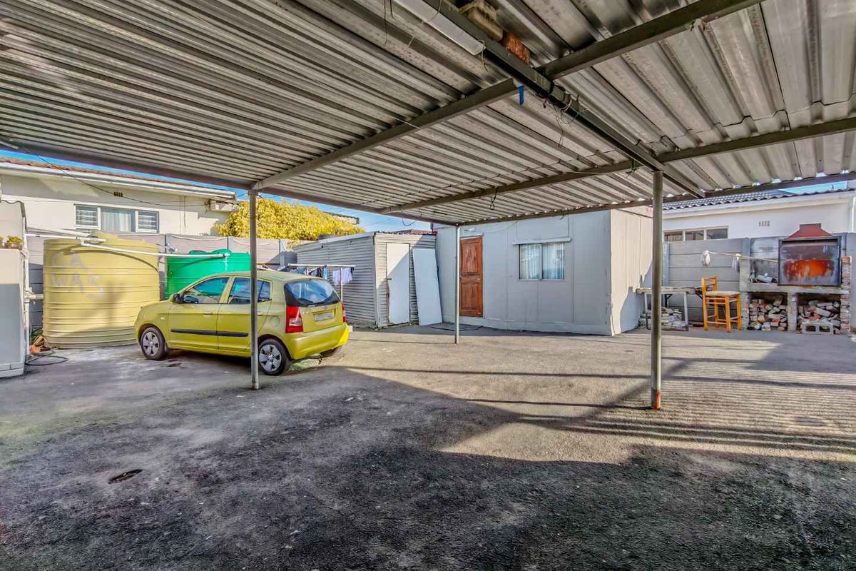 Outdoor area featuring a large metal carport structure, a built-in brick braai, and water storage tanks on a paved and unpaved yard.
