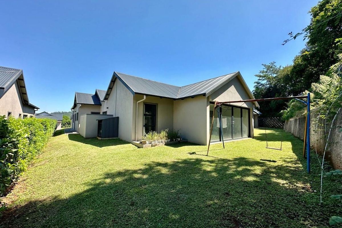 Rear view of the house featuring a well-maintained lawn, metal roof, and large sliding glass doors leading to the garden area.