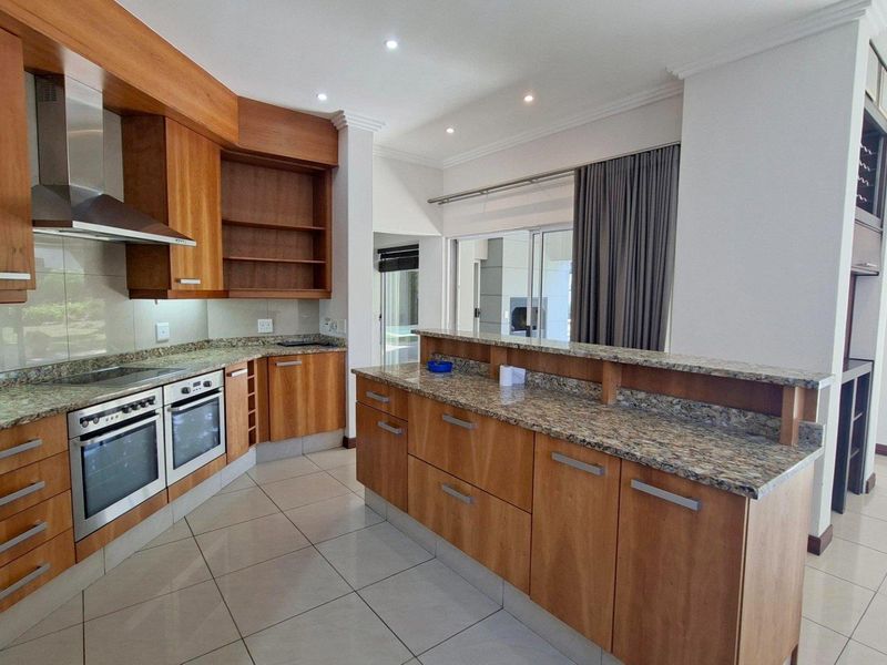 A spacious kitchen featuring wooden cabinetry, granite countertops, a double oven, and a breakfast bar, with tiled flooring and recessed lighting throughout.