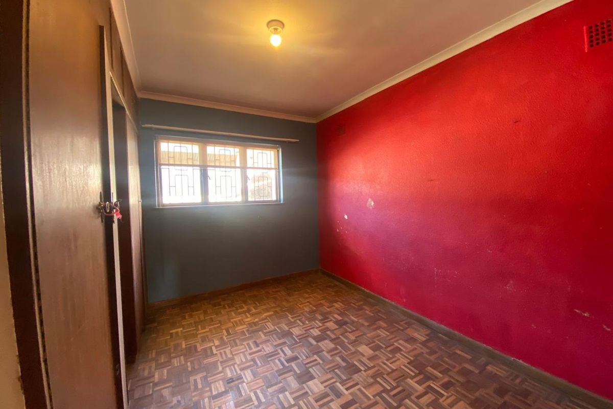 An empty bedroom featuring original parquet flooring, built-in wooden cupboards, and a window with security bars.