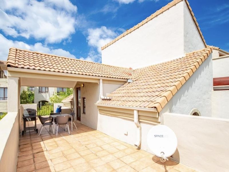 A spacious outdoor balcony featuring tiled flooring, a covered seating area, and terracotta roof tiles, providing a functional space for outdoor relaxation.