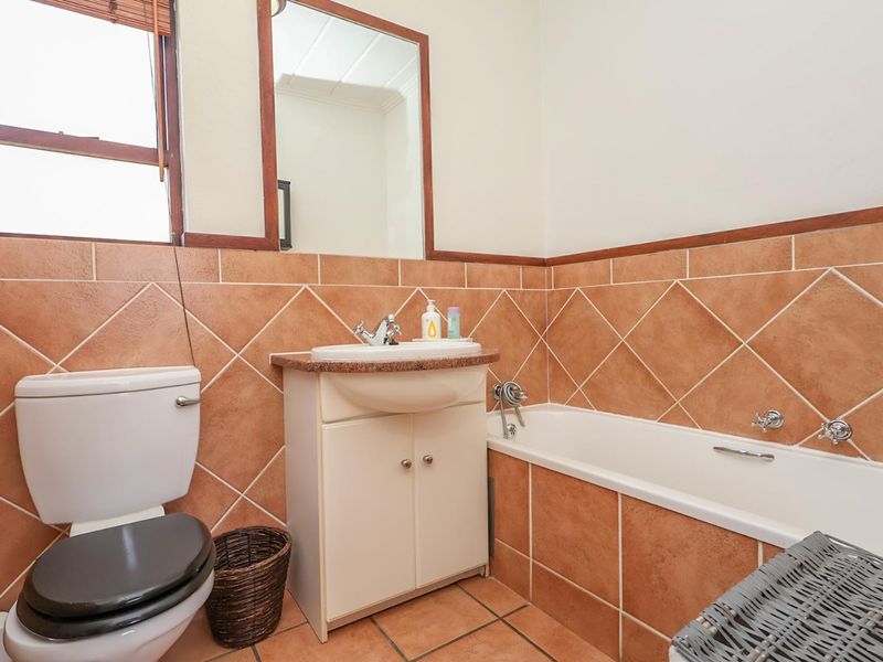 A functional bathroom featuring a vanity with basin, a standard bathtub, and a toilet, finished with terracotta-style wall and floor tiles.