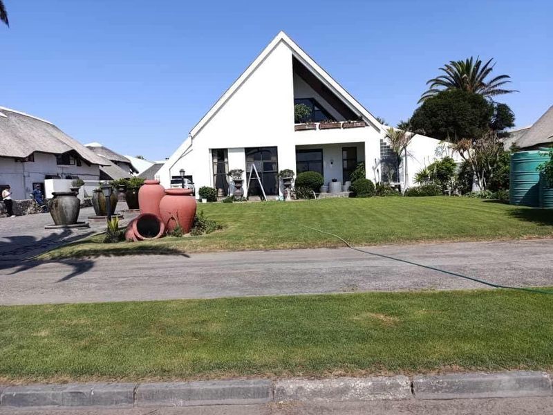 Front elevation of a modern A-frame style house featuring a manicured lawn, paved driveway, and an upper-level balcony.