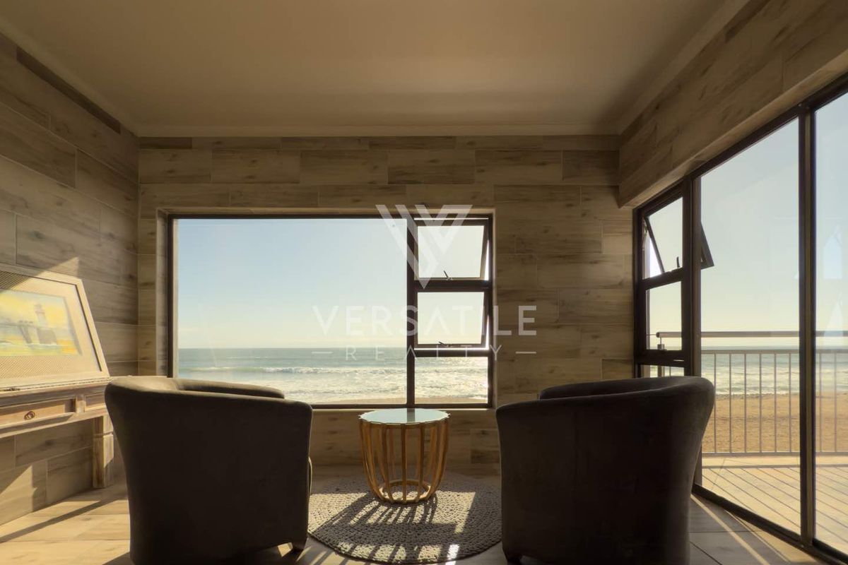 A bright living area featuring wood-look wall tiling, large windows, and sliding doors opening to a balcony with direct ocean views.