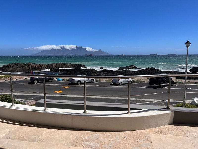 A scenic view overlooking the ocean and Table Mountain, featuring a modern stainless steel balustrade and stone-tiled patio area.