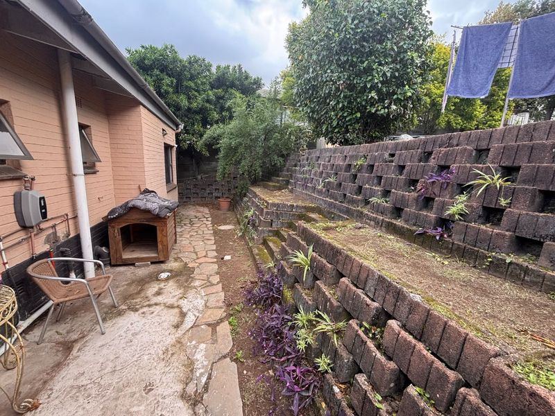 A rear exterior view featuring a stone-paved walkway alongside a multi-tiered retaining wall with integrated planting pockets.