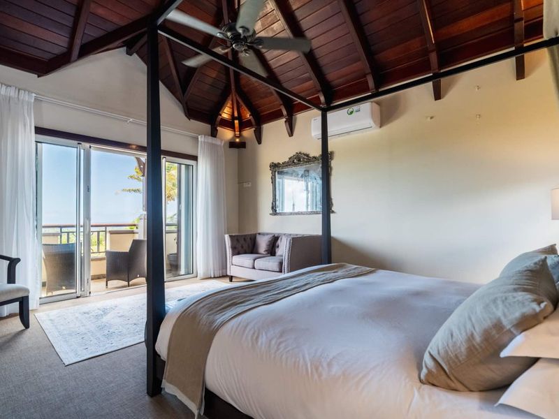 Spacious bedroom featuring a vaulted timber ceiling, ceiling fan, wall-mounted air conditioning unit, and sliding glass doors opening onto a private balcony.