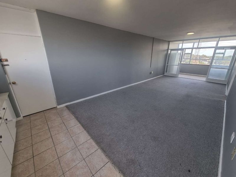 An empty, open-plan living area featuring a mix of tiled and carpeted flooring, with direct access to a balcony through glass doors.