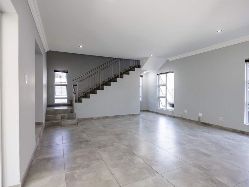 Spacious, open-plan living area featuring neutral tiled flooring, modern staircase with stainless steel balustrade, and ample natural light through large aluminium windows.