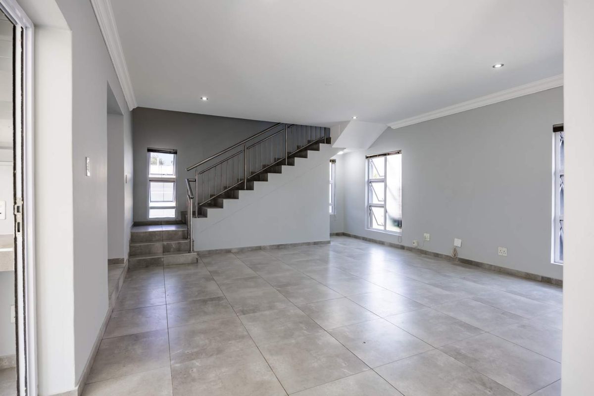 Spacious, open-plan living area featuring neutral tiled flooring, modern staircase with stainless steel balustrade, and ample natural light through large aluminium windows.