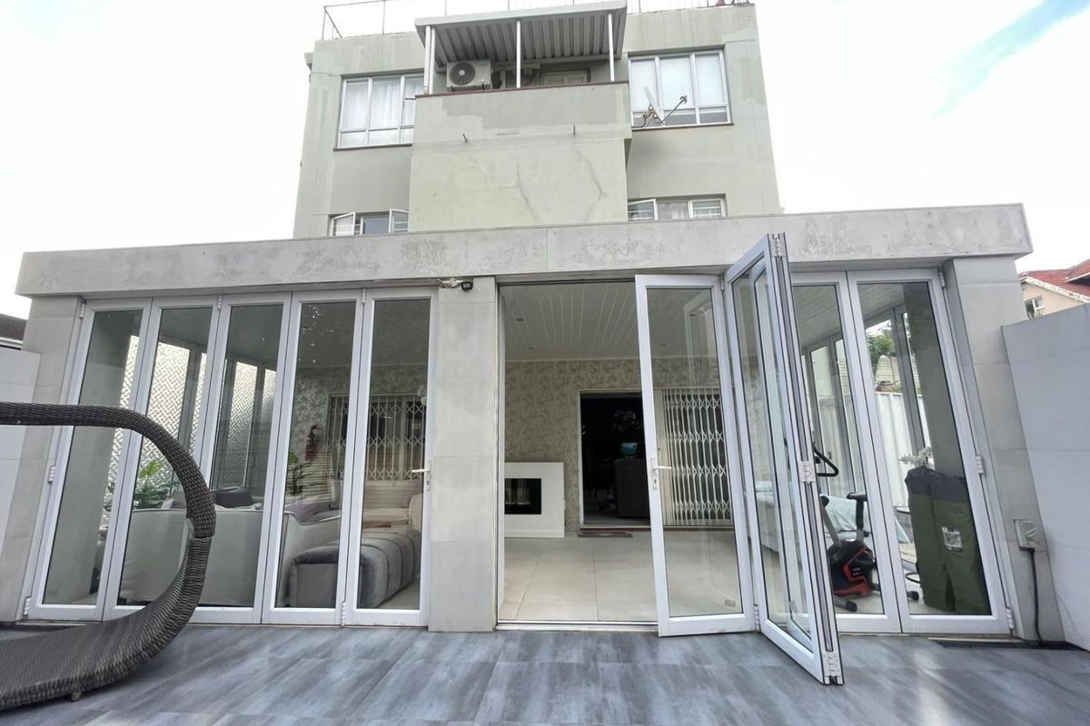 Rear view of the townhouse featuring a tiled patio, extensive bi-fold glass doors, and a built-in fireplace, showing signs of exterior wear.