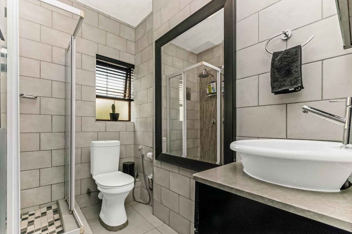 Modern bathroom featuring a glass-enclosed shower, a contemporary vessel sink on a vanity, and neutral wall tiling.