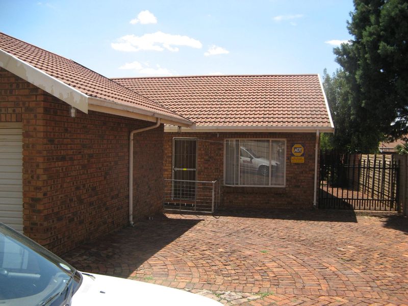 Front exterior view of a brick townhouse featuring a tiled roof, paved driveway, and secure gated entrance.