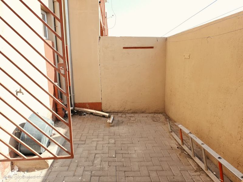 A small paved rear courtyard area featuring a boundary wall, external water tap, and drainage downpipe.