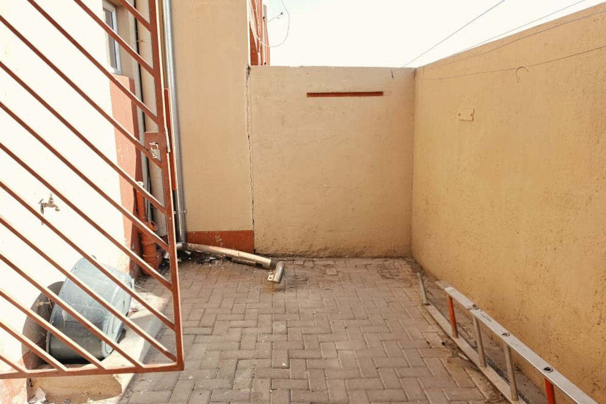 A small paved rear courtyard area featuring a boundary wall, external water tap, and drainage downpipe.