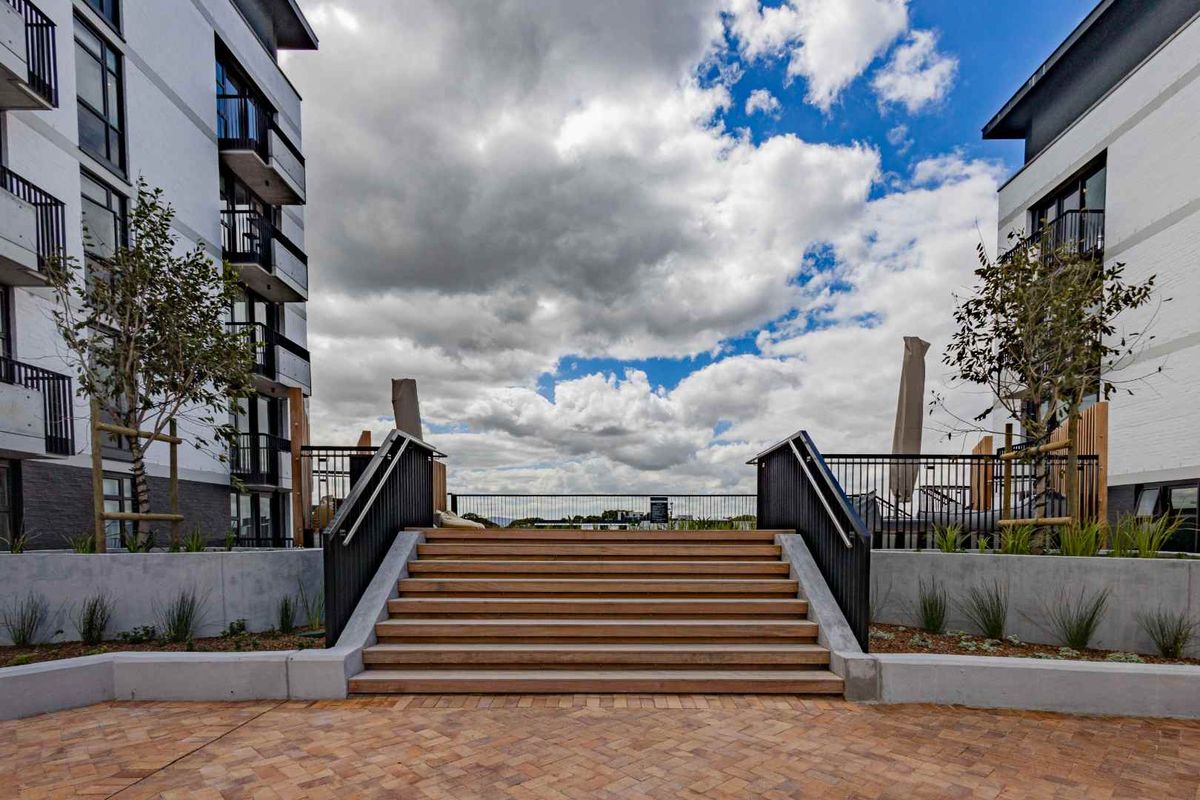 A well-maintained outdoor courtyard area featuring timber stairs, concrete retaining walls, and brick paving between modern apartment buildings.