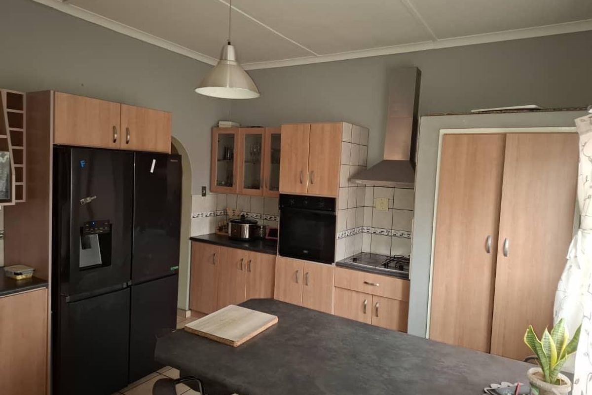 A functional kitchen featuring light wood-tone cabinetry, a built-in oven, stainless steel extractor fan, and a central island with a dark countertop.