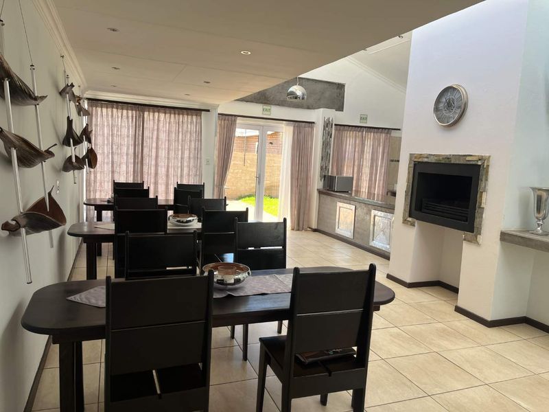Spacious open-plan dining and living area featuring a built-in fireplace with stone surround, tiled flooring, and direct access to the outdoor garden area.