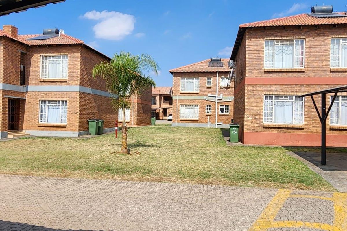 Exterior view of a residential apartment complex featuring face brick facades, tiled roofs, solar water heating systems, and a communal lawn area.